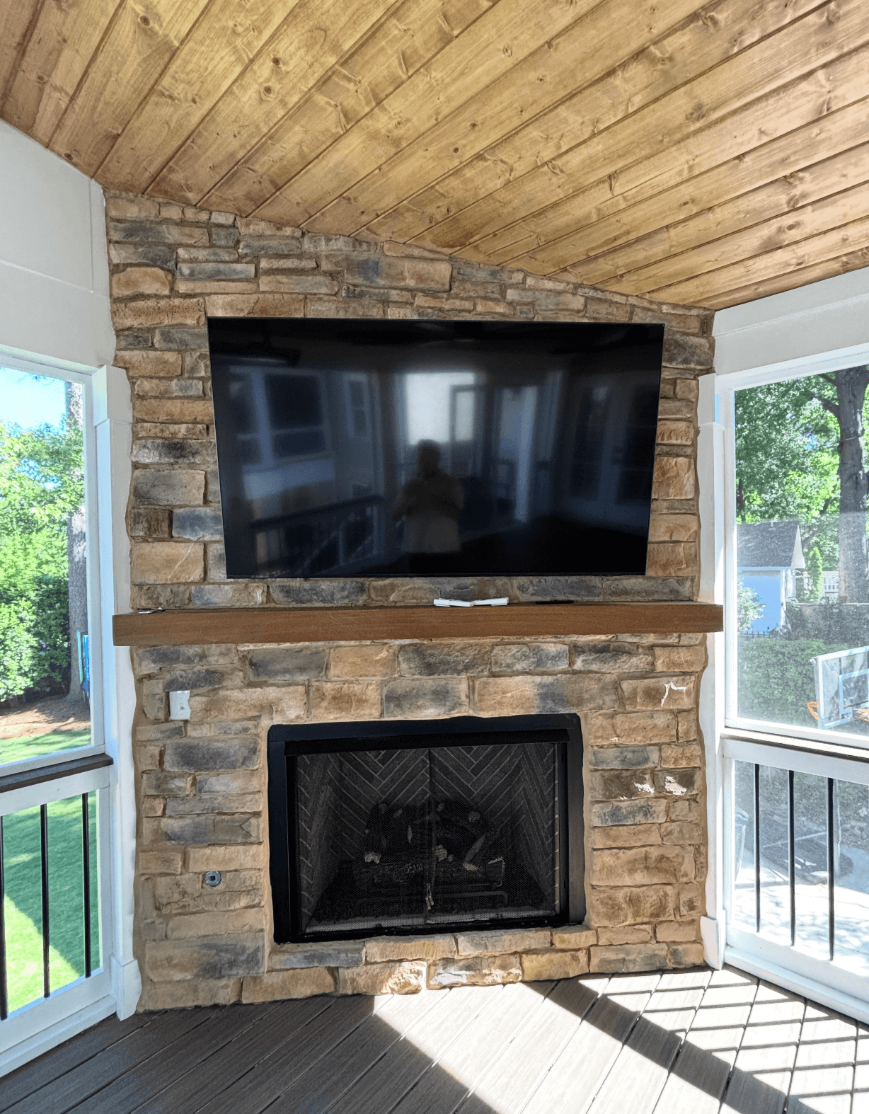 Stone gas fireplace with TV mounted above and wood mantel