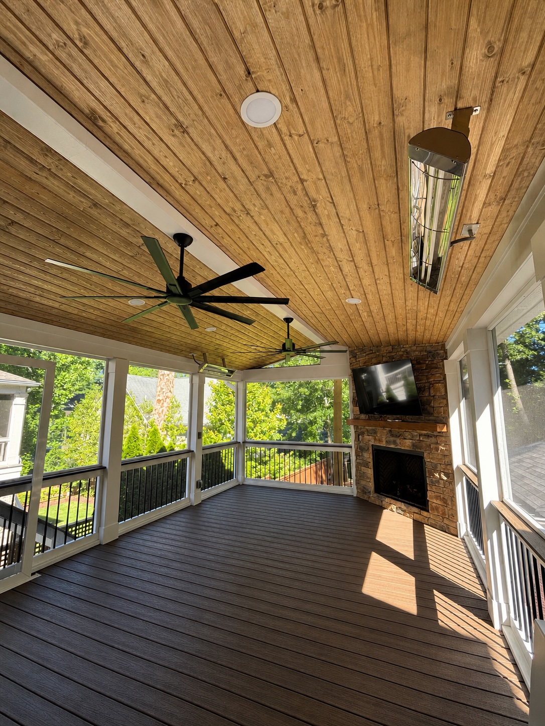 Spacious screened porch interior with tongue-and-groove ceiling, ceiling fans, and stone fireplace
