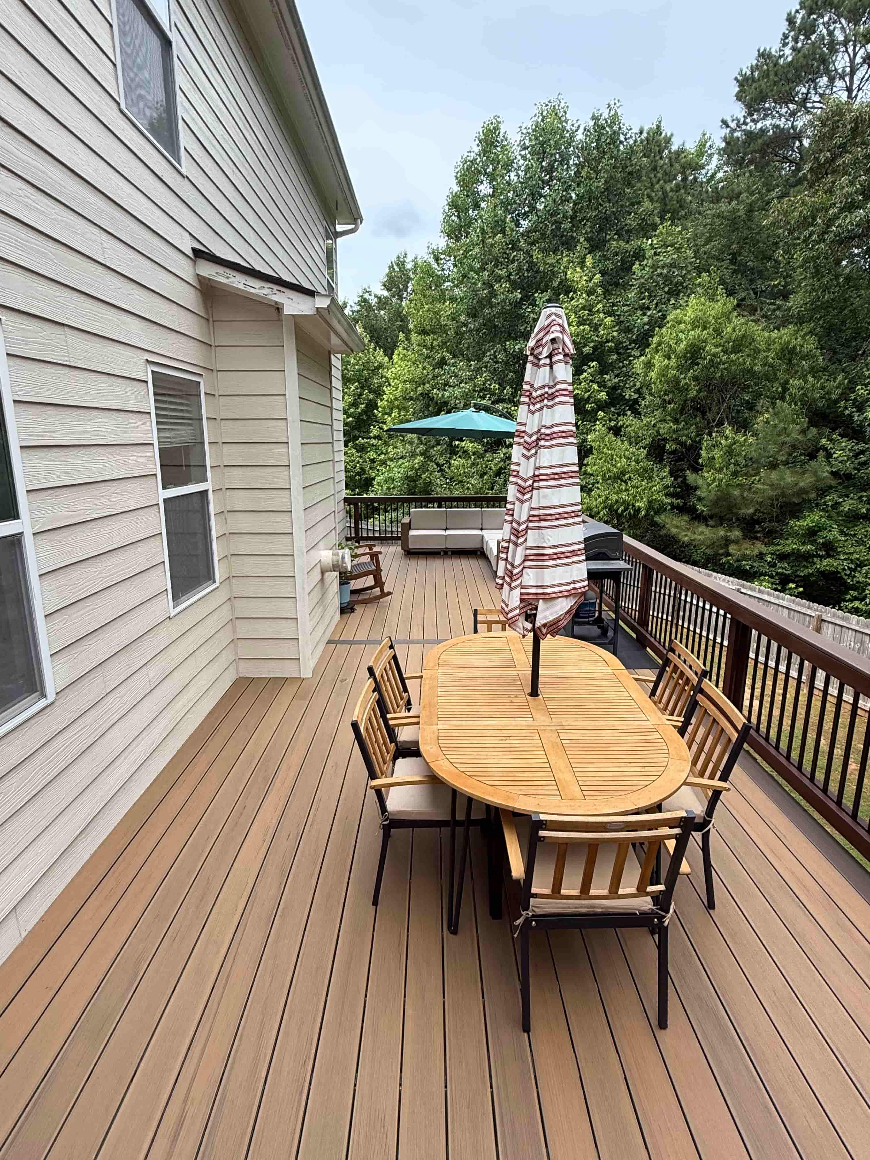 Two-tone composite deck with teak dining table and umbrella overlooking wooded backyard in Canton, GA